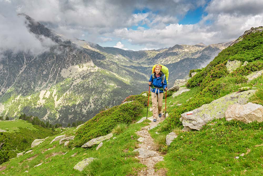 Happy woman hiker travels in Pyrenees Mountains in Andorra and Spain. Nordic walking, recreation and trekking along GR11 path trail