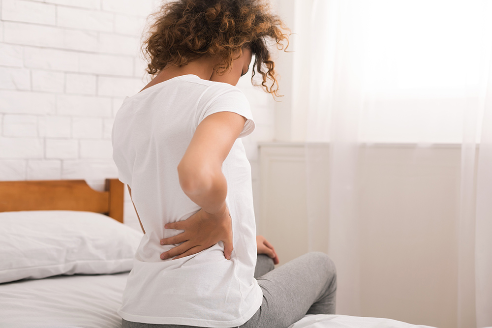African-american woman having back pain after sleep, sitting on bed